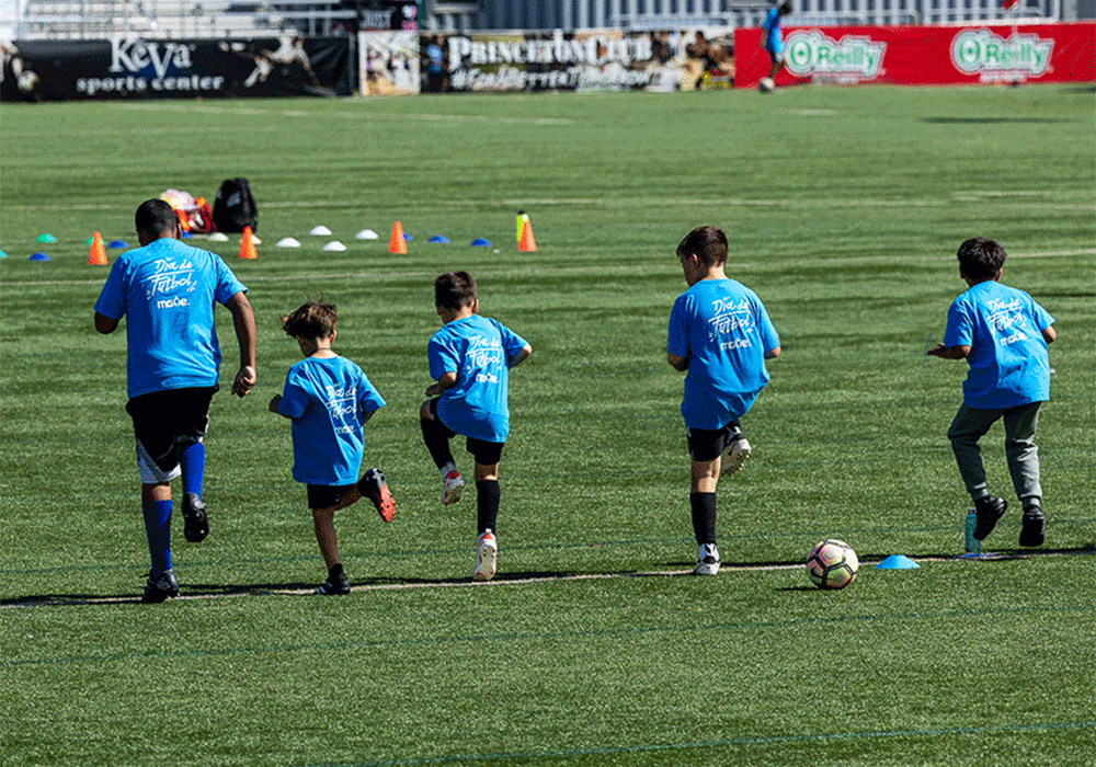 An adult and a group of children participating in a soccer clinic at MGE’s Día de Fútbol.