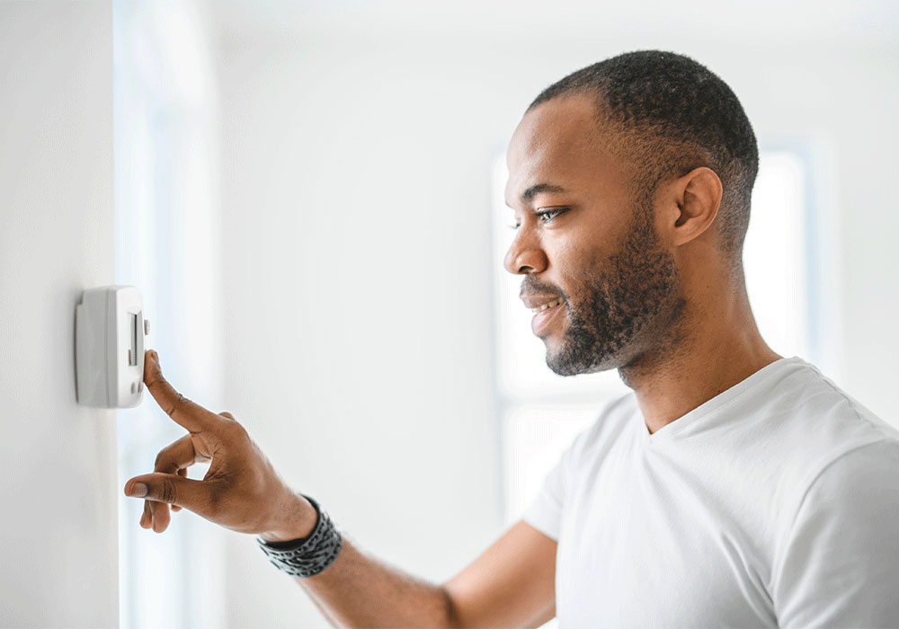 An African American man adjusts a thermostat on the wall in his home.