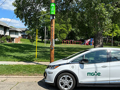 An electric vehicle (EV) parked beside a pole-mounted charger in Madison.