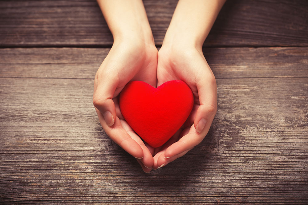 Offering a red heart in cupped hands.