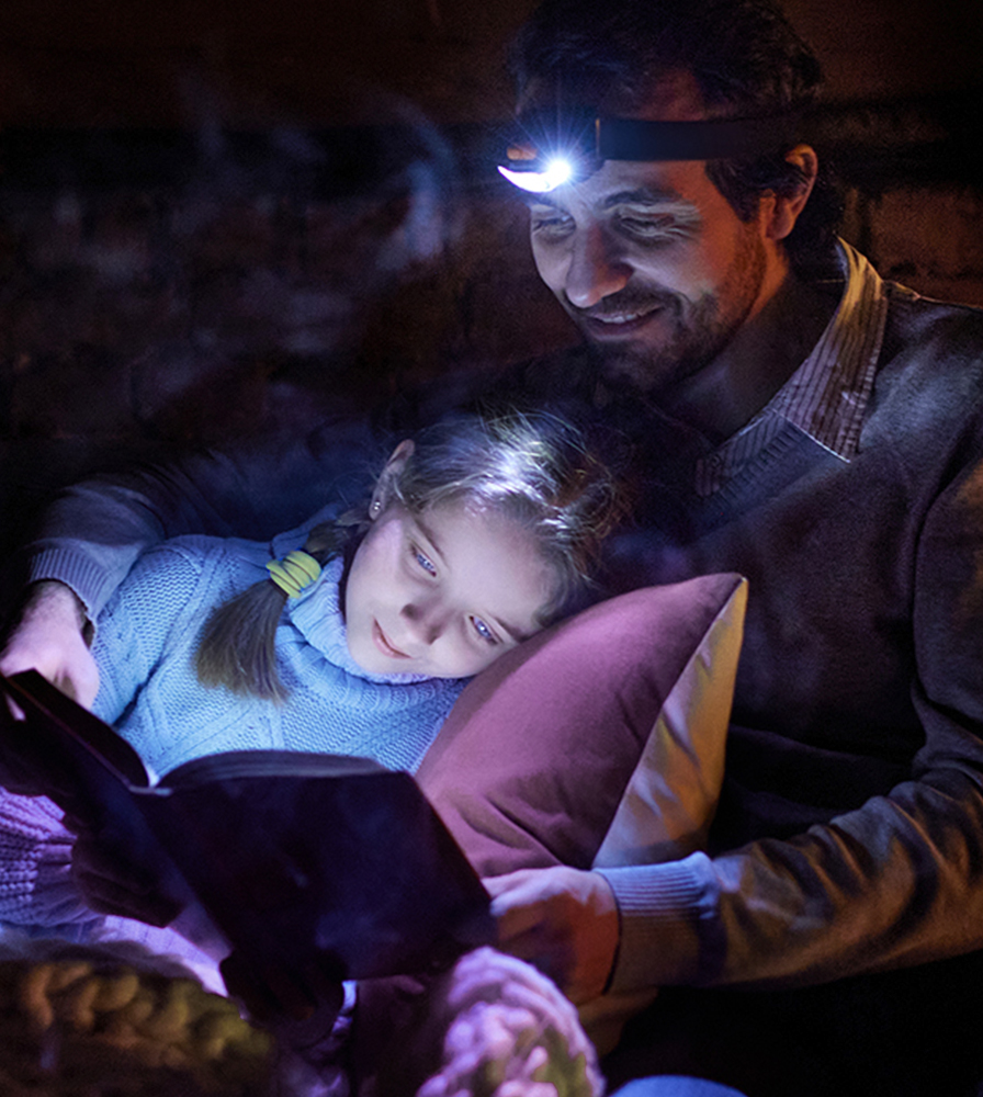 Dad reading to daughter with headlamp during power outage.