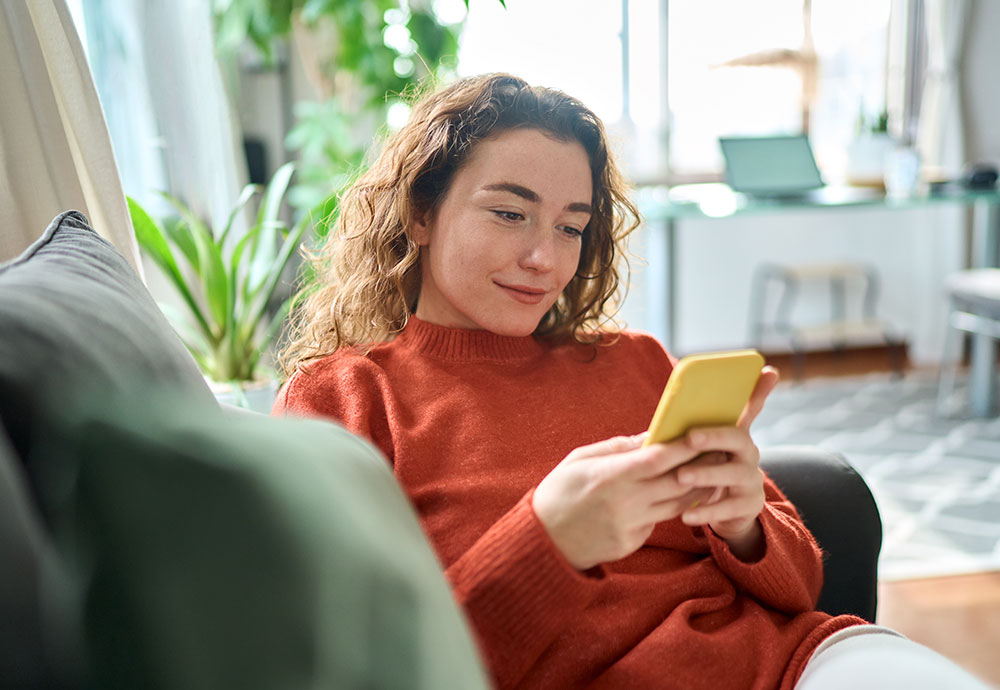 Woman reviewing information on her phone while relaxing on a couch