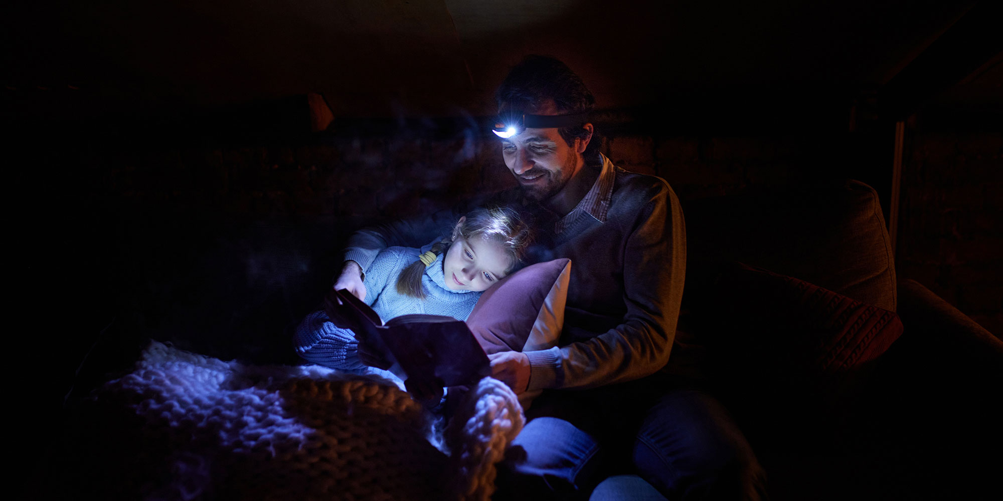 Father and child reading with headlamps during an electric outage.