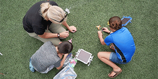 A woman and two children tinkering with a mini solar kit.